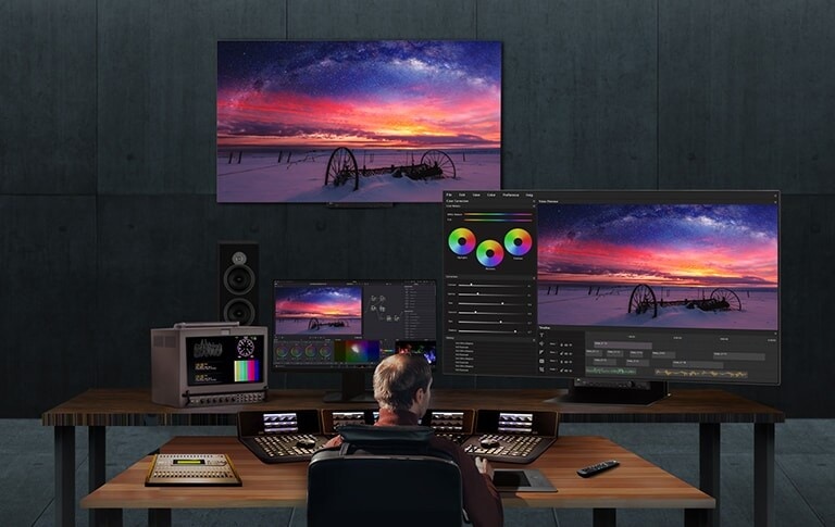 صورة يظهر بها رجل يعمل على تحرير فيديو باستخدام اثنتين من شاشات 65EP5G إحداهما مثبتة على الجدار والأخرى على المكتب في مكان عمله.