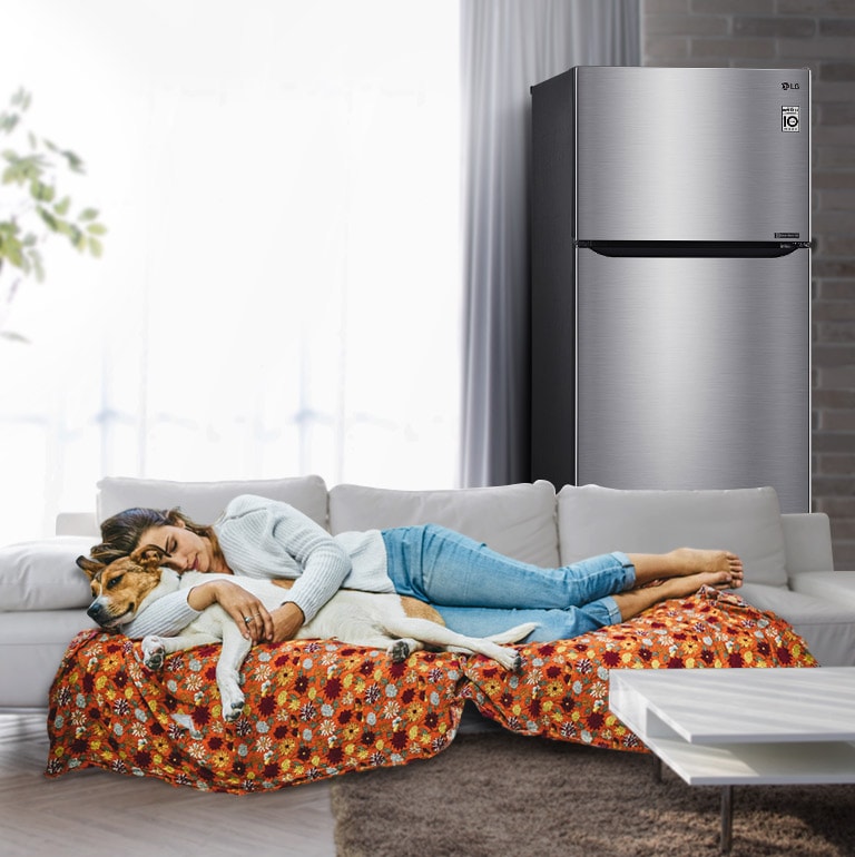 امرأة وكلب ينامان على أريكة بالقرب من الثلاجة.