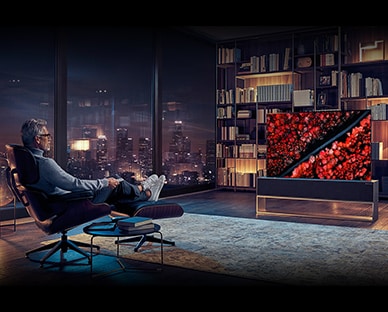  رجل يجلس على كرسيه الوثير ويضع قدمًا على أخرى بينما يشاهد تلفزيون LG SIGNATURE Rollable OLED.