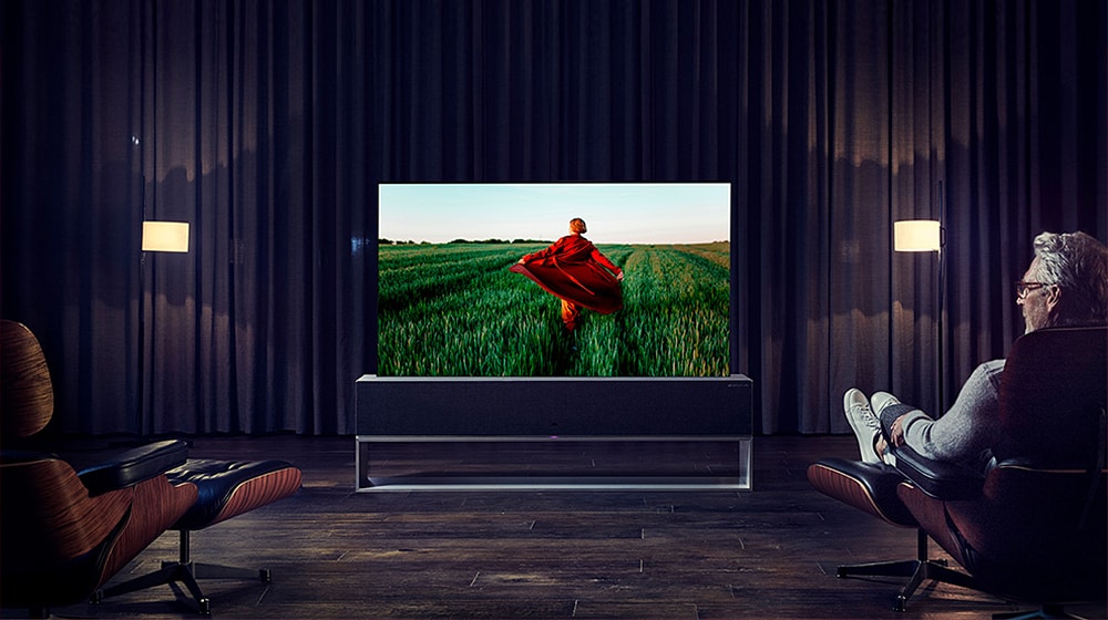 رجل يجلس على كرسيه الوثير ويضع قدمًا على أخرى بينما يشاهد تلفزيون LG SIGNATURE Rollable OLED.