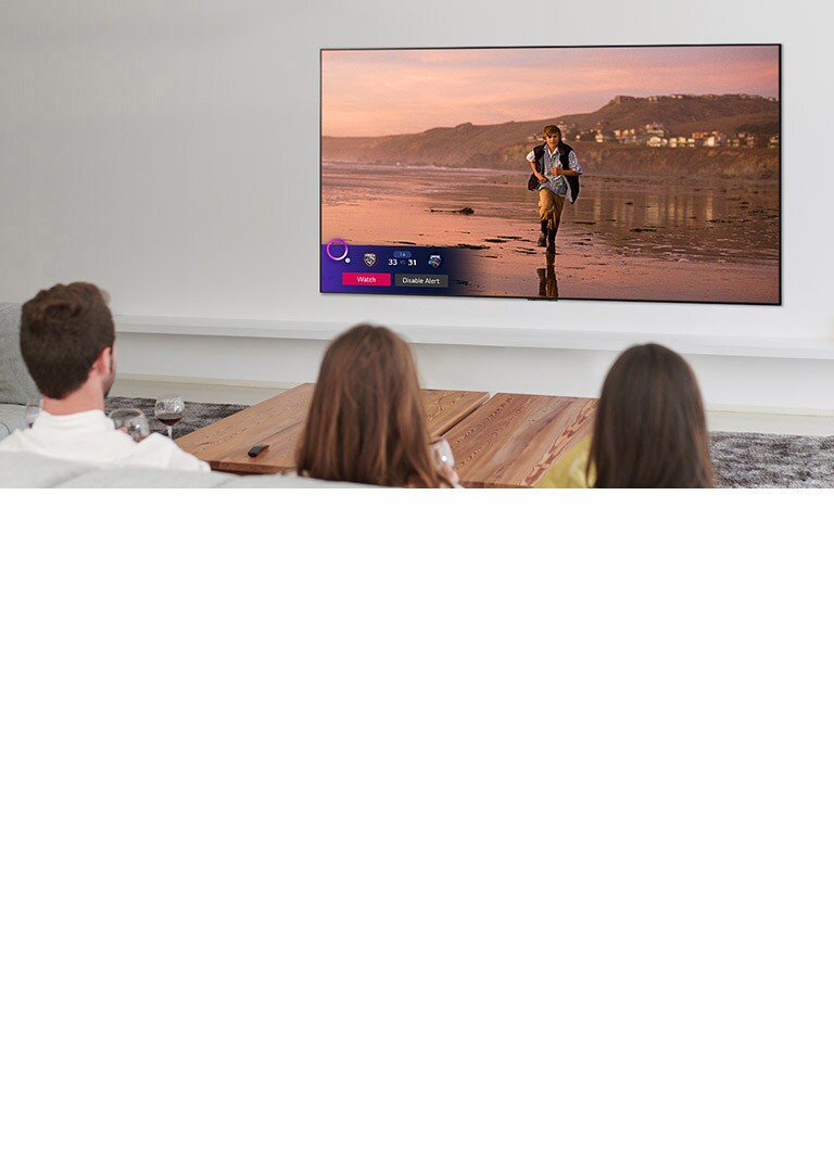 ثلاثة أشخاص يشاهدون شاشة تلفزيون تظهر مشهدًا من فيلم خيالي مع تشغيل المنبه الرياضي