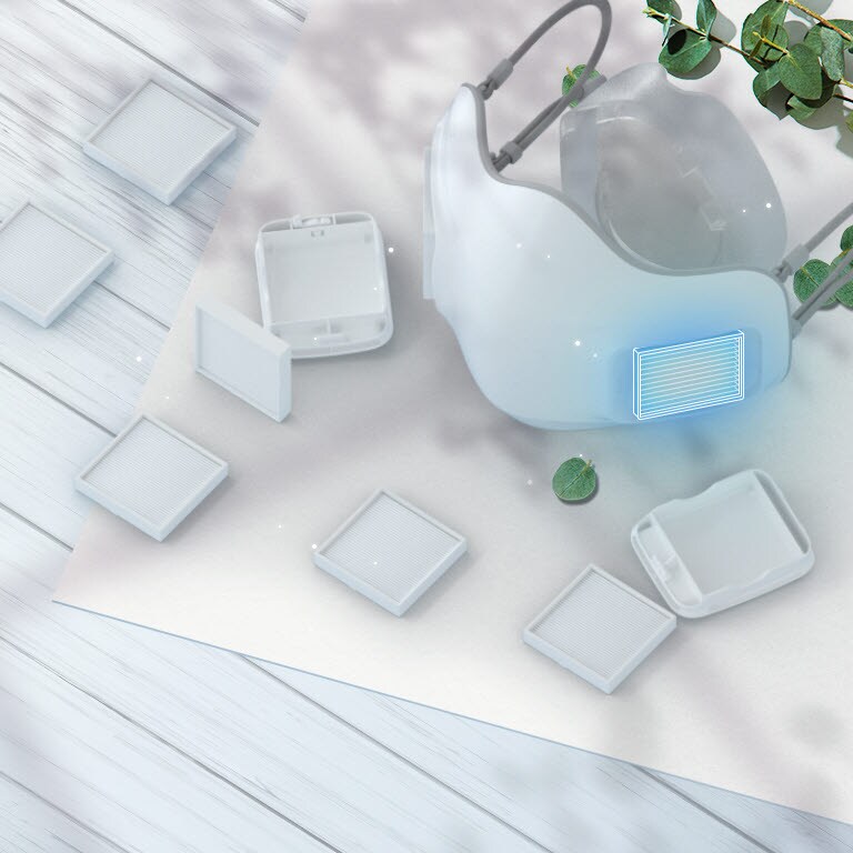 The LG PuriCare Wearable Air Purifier viewed at an angle from the top with H13 Grade HEPA filters scattered around on the table around it. The place to insert the filter on the mask is highlighted with a blue square.