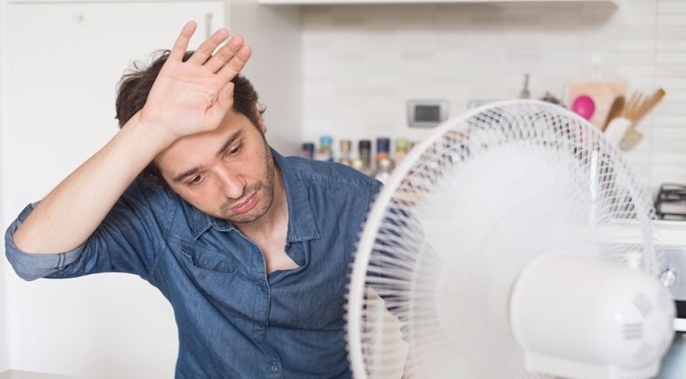A man enjoys the breeze from an electric fan