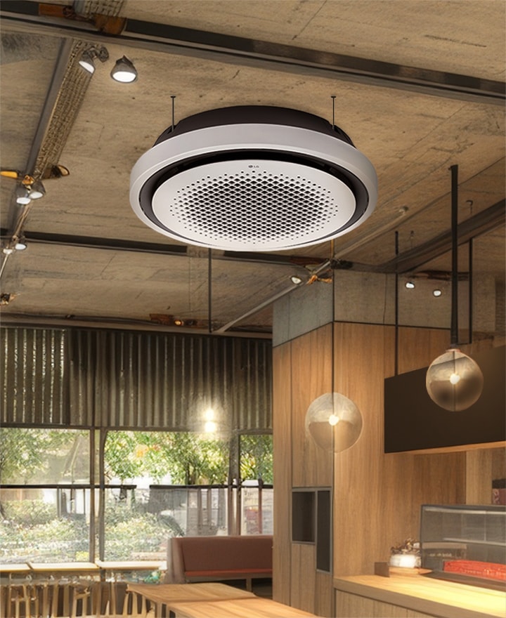 The LG Round Cassette is elegantly displayed in a modern office space, featuring its distinct round design that blends seamlessly with contemporary wooden and concrete interior aesthetics.  