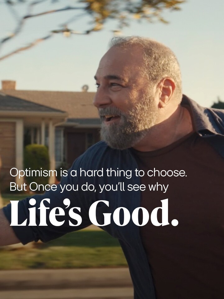 In the late afternoon, a friendly elderly person is riding down the street on a skateboard, wearing a bright smile.