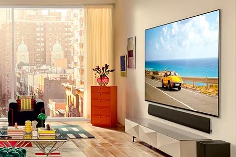 An angled view of LG OLED G3 on the wall of a city-view apartment with a Soundbar below.