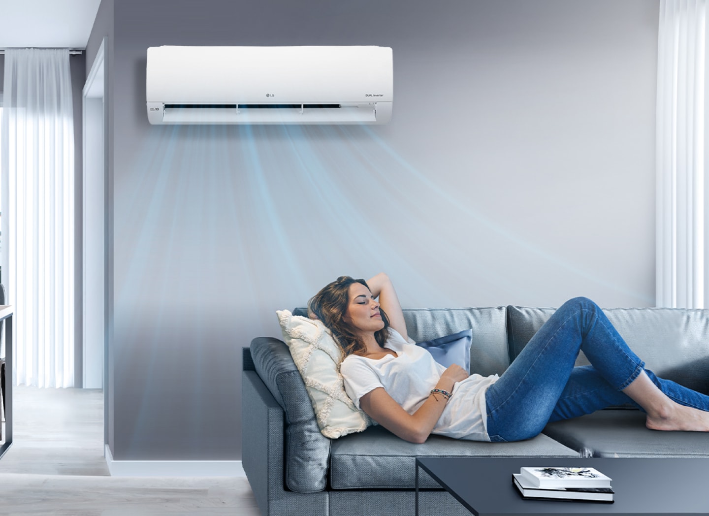 A woman lounges on a couch in a living room with the LG air conditioner installed above her on the wall. Blue streams of air are on the image to indicate it is on and cooling the room.	