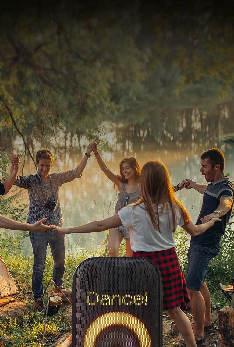 Close-up of pixel art display. It displays the Dance! Text. Below orange multi color ring lighitng is on. Behine the speaker, people are dancing on the beach.