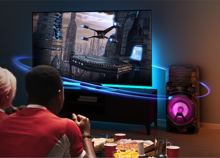 LG XBOOM RNC9 and LG TV connected by glowing wireless signals, illustrating world-first video sync control and auto-sync technology that unites screen and sound without audio lag.