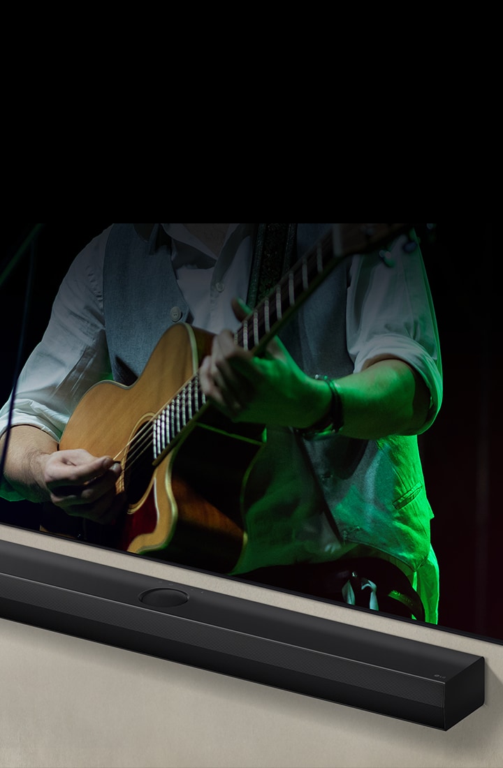 LG Soundbar against a black backdrop reveals its design starting from the left corner, then pans out to show the whole soundbar. An LG QNED TV appears. The Soundbar is against the wall with the lower screen of the TV being visible, displaying a man playing the guitar.	