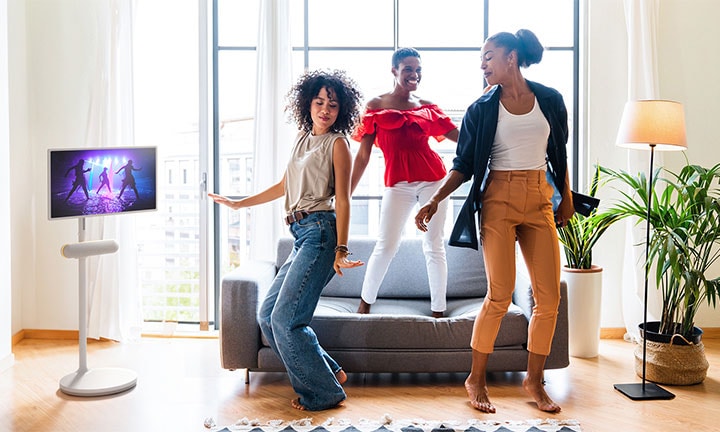 The LG StanbyME is placed in the living room with the XT7S speaker attached. People enjoy the music with the screen and speaker combo.