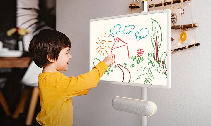 The LG StanbyME is placed in the kitchen with the XT7S speaker attached. A child draws on the screen, and the speaker's yellow mood lighting is on.