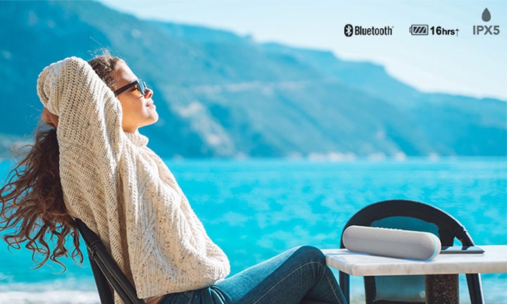 A woman enjoying music on the outdoor terrace with LG XT7S speaker.