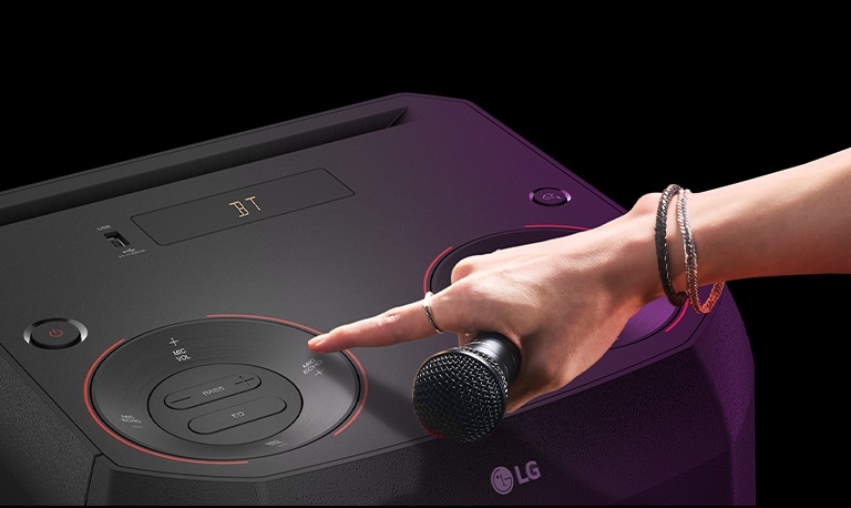 A hand holding a microphone tries to press the MIC ECHO button on the top of the speaker.