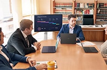 Four people are sitting around a desk, having a meeting using a LG Smart Monitor Swing.