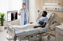 A patient is lying in a hospital bed, with two medical professionals standing beside them. A LG Smart Monitor Swing is next to the doctor.