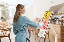 A woman is looking at an event banner displayed on a LG Smart Monitor Swing in a café.