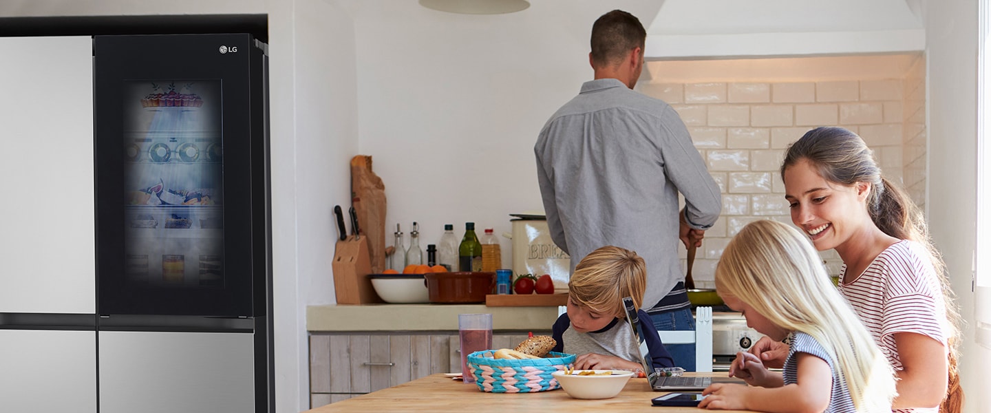 Family is sitting at the table for a meal. InstaView refrigerator installed on one side of the kitchen
