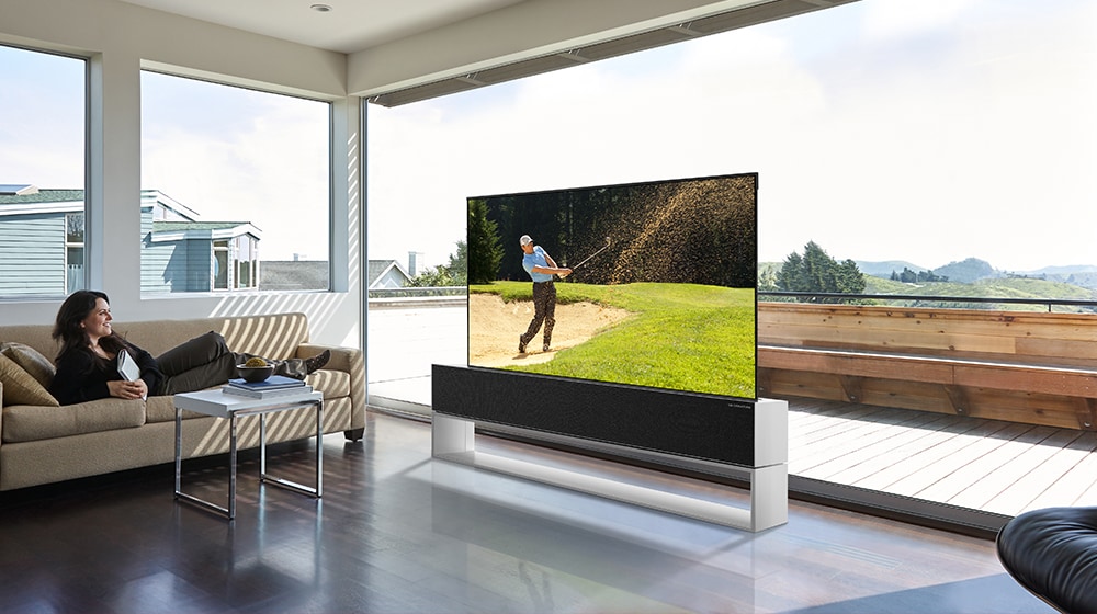 A woman is sitting on a couch while watching TV showing a golf player playing golf.