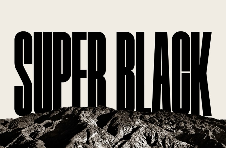 The words "SUPER BLACK" appear in bold black capitals. A black mountainous scene with crisp definition then rises to cover the letters, also revealing a village and sand dunes. The black copy disappears behind a black sky.	