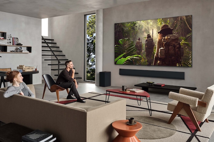 Wide view of a living room inside a premium home, a man is watching a movie on his wall-mounted LG OLED TV. The TV's design blends elegantly with the wall and the interior design.