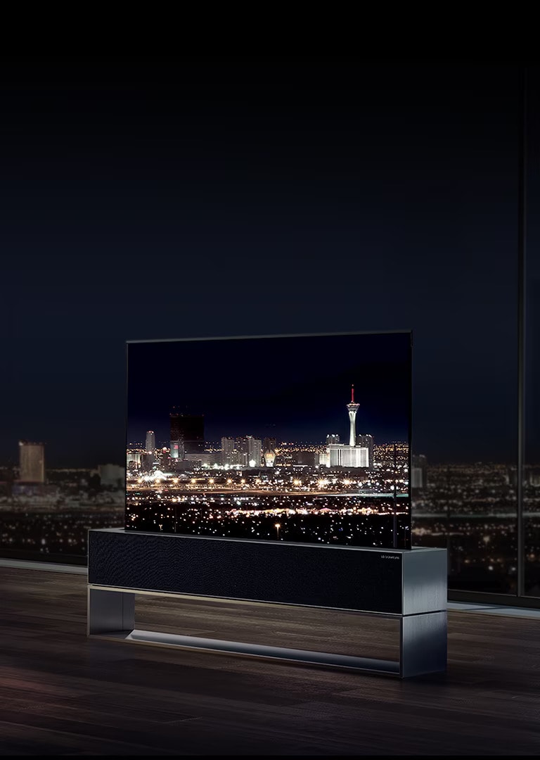A man watches LG SIGNATURE's Rollable OLED TV facing the night city view of Las Vegas in his living room.