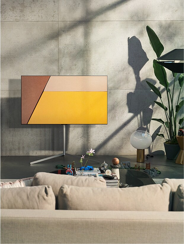 An LG OLED television is in a modern gray living space against a window showing a swimming pool. An LG OLED television is in a neutral living space with exposed bricks, wooden details, and greenery.