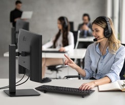En kvinna bär ett headset och arbetar medan hon tittar på en bildskärm.