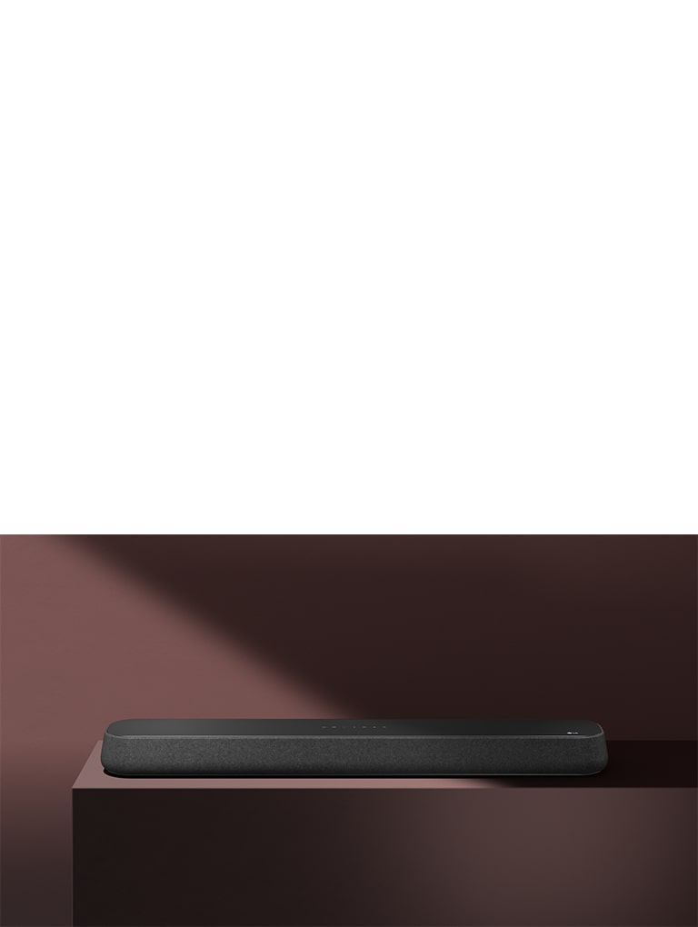 LG Sound Bar SE6S står på en röda låda framför en röd bakgrund. En svart skugga täcker den övre högra halvan av bilden.