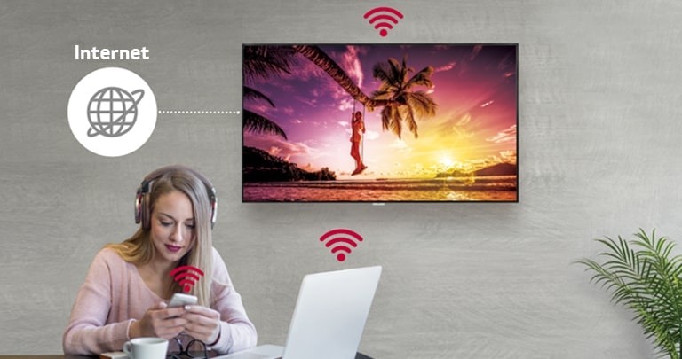 UM3DG-H-serien finns på väggen och en kvinna använder en PC och en mobiltelefon. Och den här bilden visar att den digitala skylten kan kopplas trådlöst till PC:n och till mobilen som hon håller i.