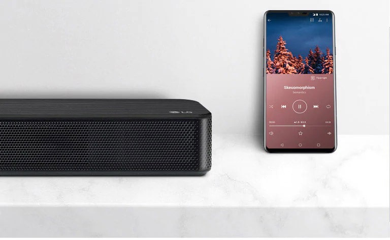 Närbild av höger sida av LG Soundbar bredvid en smartphone. Det finns två enheter på den vita hyllan.