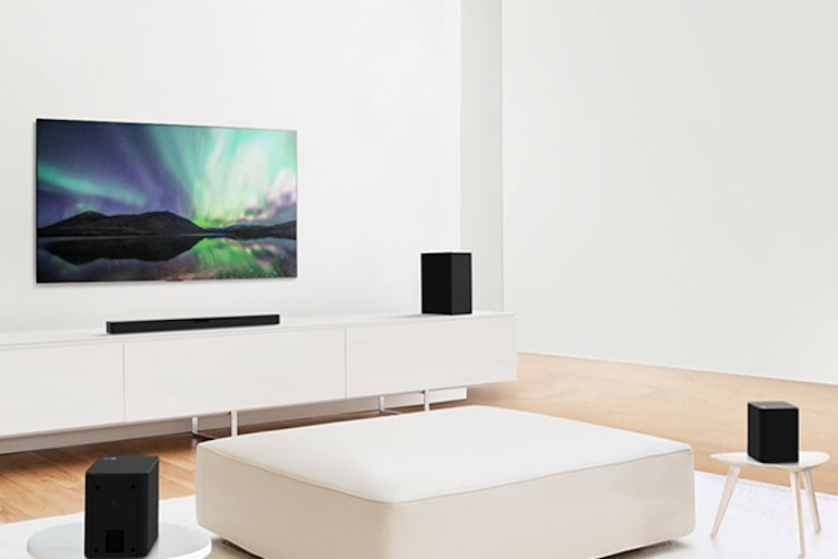 TV och sound bar i ett vitt vardagsrum med vit soffa i mitten. Högtalare sitter i båda ändarna av soffan.