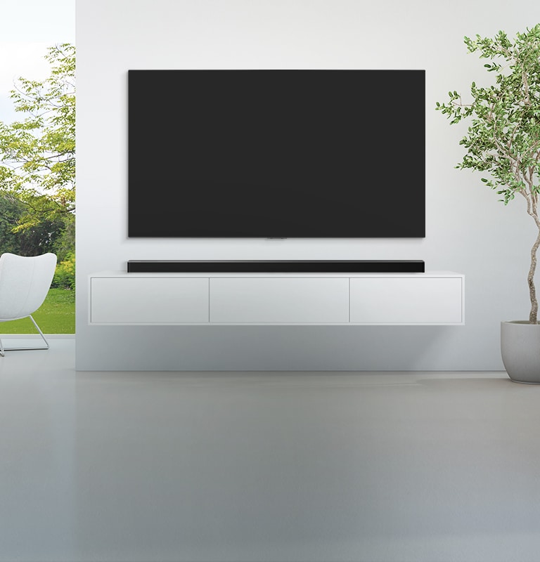 En TV och en soundbar står i ett stort vardagsrum som går i vitt, och utanför det stora fönstret finns en utsikt över en grön skog. 