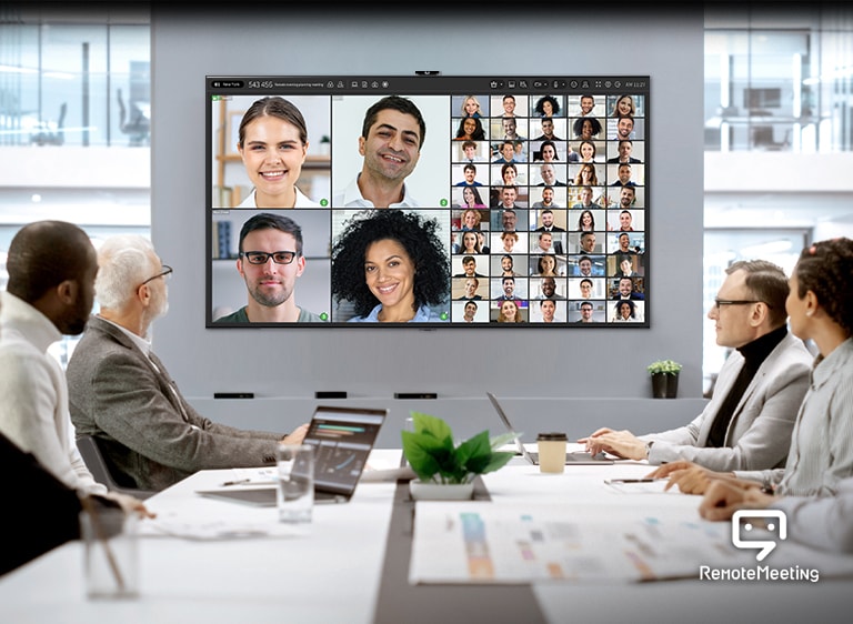 Människor är samlade i ett konferensrum och har en videokonferens via Remote Meeting-appen på TV:n.