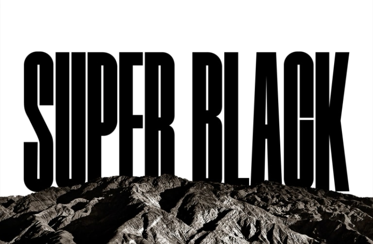 Orden ”SUPER BLACK” visas med svarta versaler. En svart bergsscen med skarp definition stiger sedan upp för att täcka bokstäverna och avslöja en by och sanddyner. Den svarta kopian försvinner bakom en svart himmel.