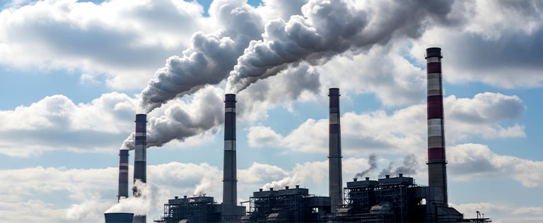 An image of several factory chimneys emitting chemicals and greenhouse gases in the cloudy sky.