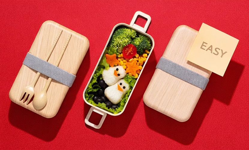 An image showing an easy bento box meal with penguin-shaped rice balls and colorful vegetables on a red background, illustrating a simple meal-prep concept.