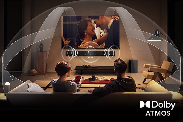 Dimly lit, cozy living room with an OLED LG TV with LG Soundbar. On the screen is a close-up of an electric guitar being played. Graphics show how Dolby Atmos fills the whole space with surround sound from all directions. Dolby Atmos logo is at the bottom corner.