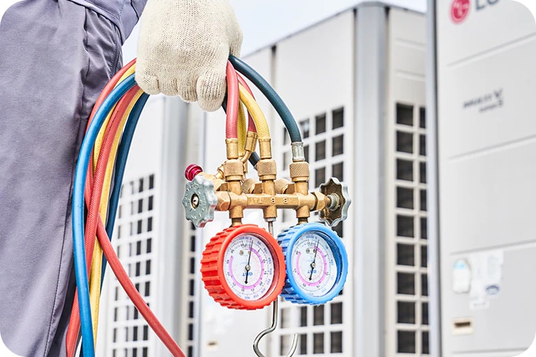 One person is standing in front of the outdoor units with the refrigerant manifold gauge.