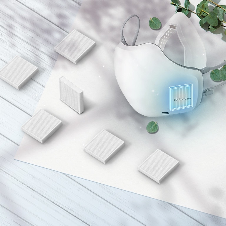 The LG PuriCare Wearable Air Purifier viewed at an angle from the top with H13 Grade HEPA filters scattered around on the table around it. The place to insert the filter on the mask is highlighted with a blue square.