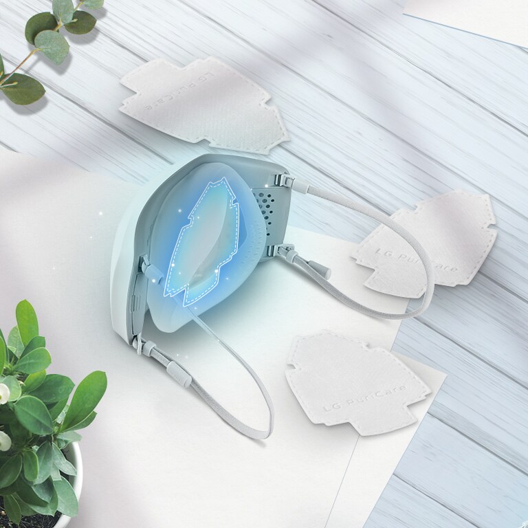 The LG PuriCare Wearable Air Purifier viewed at an angle from the top with H13 Grade HEPA filters scattered around on the table around it. The place to insert the filter on the mask is highlighted with a blue square.