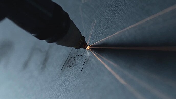 Interface icon of LG SIGNATURE Refrigerator is being carved by a tool on its stainless steel body.