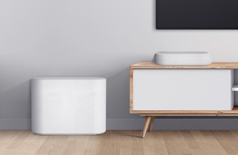 LG Eclair is placed on a wooden, white cabinet and a subwoofer is placed right next. A bottom left corner of TV is shown.