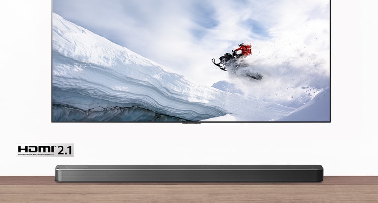 TV and Soundbar are seen from the front. TV shows man riding snowmobile in the snowy mountains. HDMI 2.1 logo is below TV.