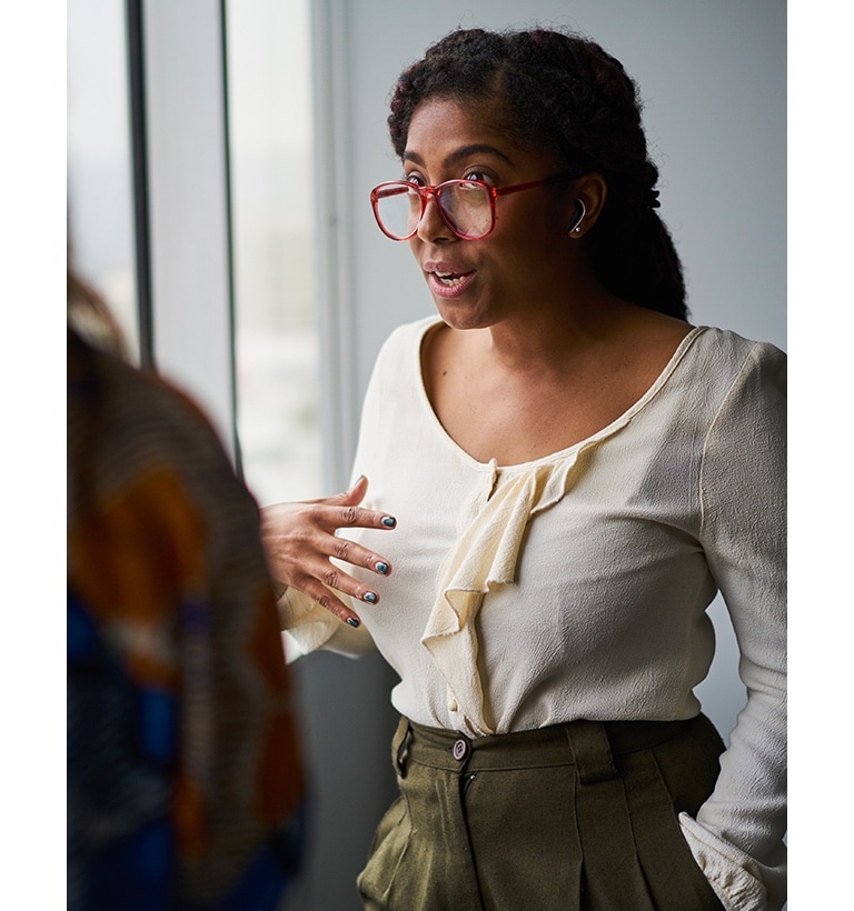 Two women are talking. The woman facing out is wearing the earbuds.