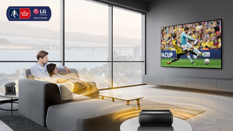 A man and women watching sports game on TV in the living room with Bluetooth rear speakers