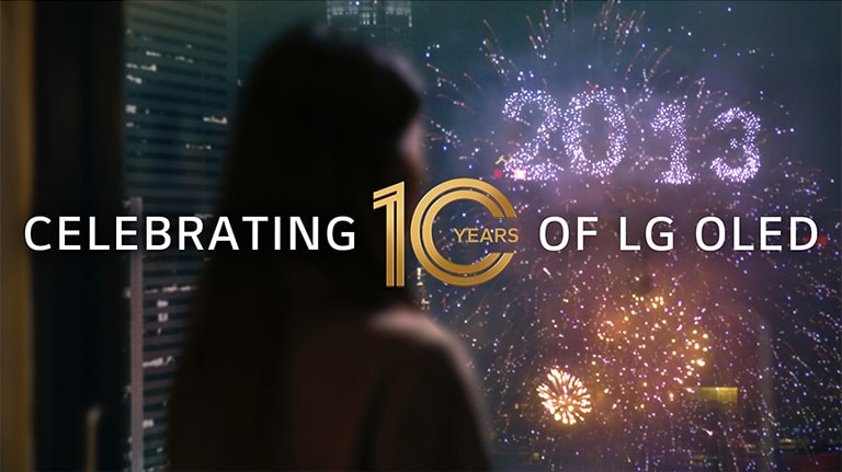 女性が、2013 と空に描かれる花火を窓から見ている。オーバーレイのテキストに「祝 LG 有機 EL テレビ 10 周年」と書かれている。