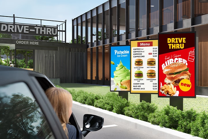 Outdoor displays are installed in the drive-thru zone of the burger place, vividly showing menus and images even in bright sunlight.