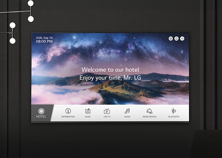 A wall in a dimly lit room features an LG TV, displaying a welcome message using the LG Pro:Centric Direct solution.	