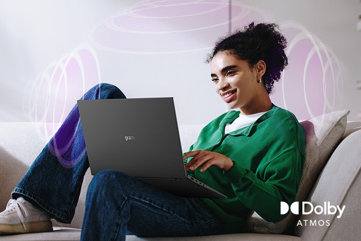 A person sitting on a couch, enjoying immersive audio while using an LG gram laptop. The text highlights Dolby Atmos technology, emphasizing a rich, expansive, 360-degree auditory experience. Surrounding sound waves in the background visually represent the immersive soundscape.